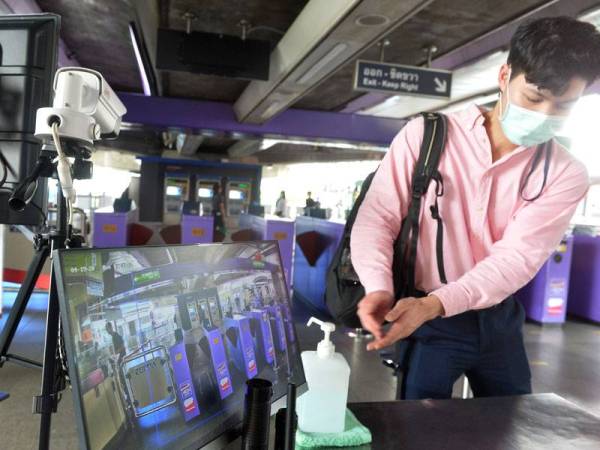 Seorang lelaki memakai pelitup muka berjalan ke stesen skytrain BTS di Bangkok. - Foto Xinhua