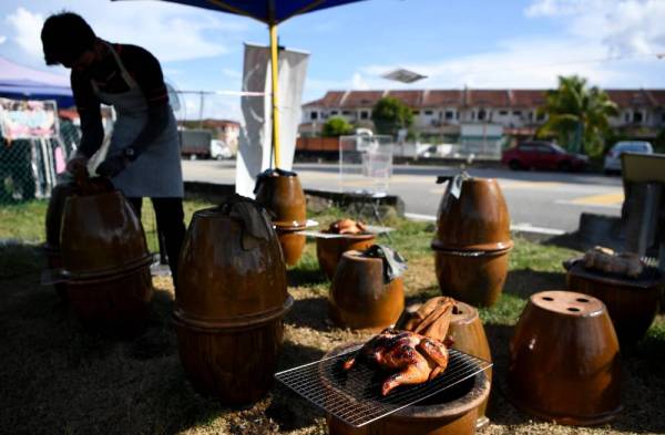 Harith Iskandar melihat ayam yang sedang dibakar menggunakan arang di dalam pasu supaya tidak rentung ketika berniaga di tepi jalan utama ke Kampung Tengah pada Selasa. - Foto Bernama