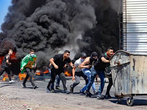 Sekumpulan pemuda Palestin menggunakan tong sampah sebagai 'perisai' mereka ketika berdepan dengan pasukan keselamatan rejim Zionis berhampiran pos pemeriksaan Hawara di bandar Nablus di Tebing Barat pada Jumaat. - Foto: AFP