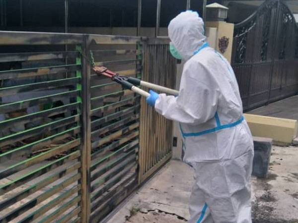 Pasukan bomba memakai sut PPE membantu membuka pintu rumah untuk membawa keluar mayat lelaki warga emas di Taman Ipoh, Ipoh pada Ahad. - Foto: Ihsan Bomba