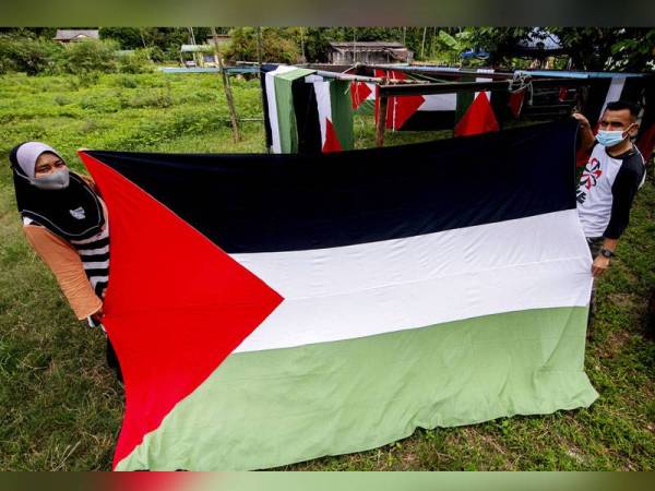 Yuslinawati (kiri) bersama sepupunya, Wan Hafizul menunjukkan bendera Palestin yang telah ditempah oleh pelanggan ketika ditemui di rumahnya di Kampung Baru Salor. - Foto Bernama