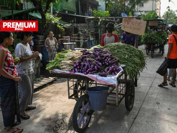 Beberapa orang melihat seorang peniaga sayur-sayuran menolak kereta sorongnya di Yangon, Myanmar baru-baru ini. - Foto AFP