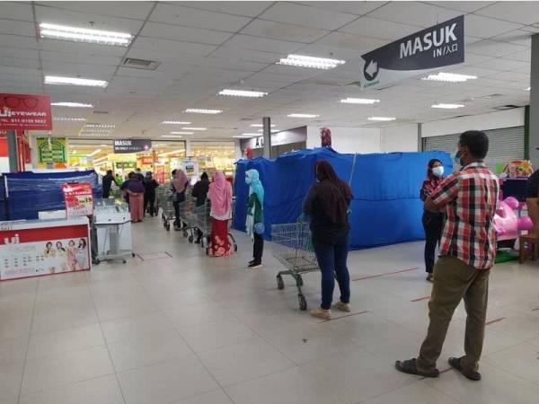 Orang ramai beratur menunggu giliran untuk membeli barangan keperluan di sebuah pasar raya di Klebang, pada Sabtu.