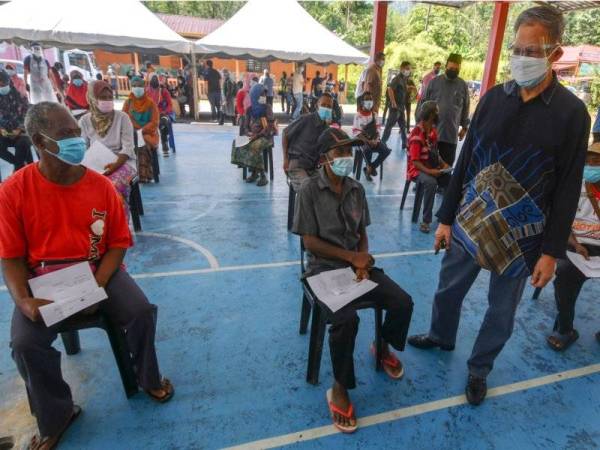 Mustapa(tiga, kiri) beramah mesra bersama sebahagian penduduk Orang Asli ketika menunggu giliran untuk menerima suntikan vaksin pada Program Outreach Vaksinasi Covid-19 di Kampung Sungai Rual, pada Sabtu. -Foto Bernama