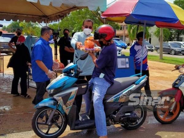 Mohd Rafiq menyampaikan telur dan ayam percuma kepada seorang penunggang motosikal di Kedai Prihatin Rakyat - Pandu Lalu Perikatan Nasional Melaka di Taman Rambai Jaya pada Isnin.