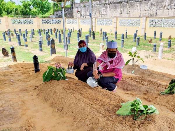 Adnan (kanan) menyiram air mawar di pusara ayahnya selepas selesai dikebumikan petang pada Ahad.