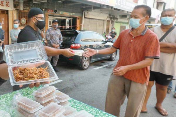 Asmadi membantu mengagihkan makanan sarapan pagi kepada komuniti lorong Wong Ah Jang di sini pada Rabu.