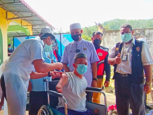 Mahu Sain teruja menerima suntikan vaksin dos pertamanya sambil disaksikan oleh Abdul Latiff (dua dari kanan) di PPV Masjid Kampung Pasir Kelang, Kuala Krai pada Rabu.