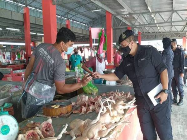 Ahmad Adnan (kanan) memeriksa MySejahtera peniaga memastikan mereka melakukan imbasan kod QR sebelum masuk ke Pasar Awam Teluk Intan ketika operasi pada Rabu.