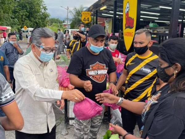 Azizul Kama (kiri) mengagihkan ikan segar kepada orang ramai sambil diperhatikan Mohd Salorwadi (dua dari kanan) ketika program berkenaan di Kampung Tersusun Tawas Tambahan, di sini, pada Jumaat.