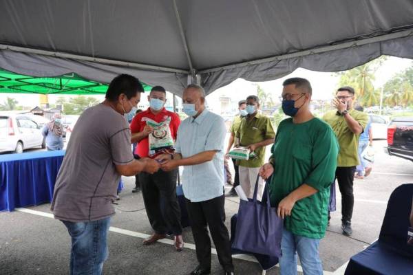 Asman (tengah) menyampaikan sumbangan kepada seorang penjaja selepas gerai rosak dipukul ribut di Taman Rinting, Pasir Gudang pada Jumaat.