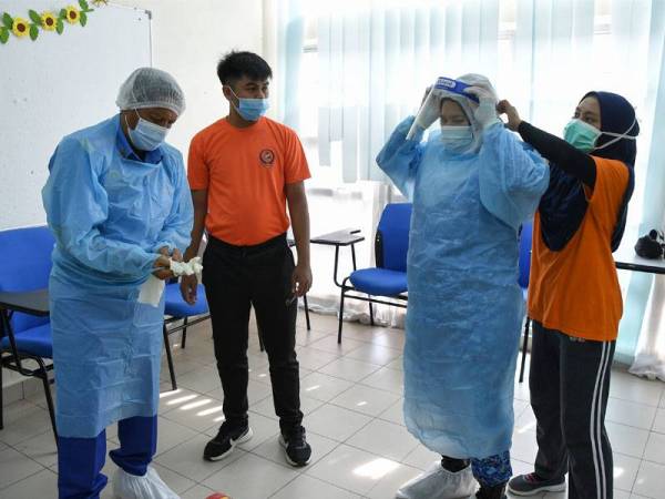 Tuan Mohd Khosim (kiri) bersama rakan setugasnya memakai PPE sebelum menghantar barangan keperluan kepada penghuni pusat kuarantin Covid-19 di IPG Kampus Dato’ Razali Ismail. - Foto Bernama