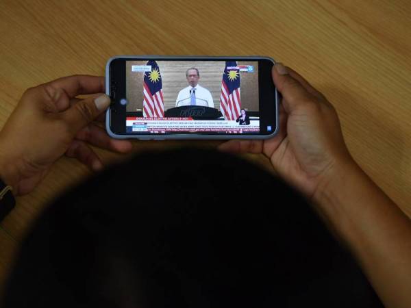 Orang ramai menyaksikan perutusan Perdana Menteri melalui telefon pintar pada pengumuman khas Pemulih yang disiarkan secara langsung melalui stesen televisyen tempatan, hari ini. - Foto Bernama