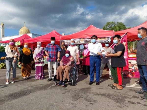 Izhar (tiga kanan) diiringi Che Zakaria (empat dari kiri) menghulurkan sumbangan kepada peniaga yang terjejas selepas gerai mereka dipukul ribut di tapak penjaja berhampiran Masjid Taman Rinting, Masai, Pasir Gudang pada Selasa.