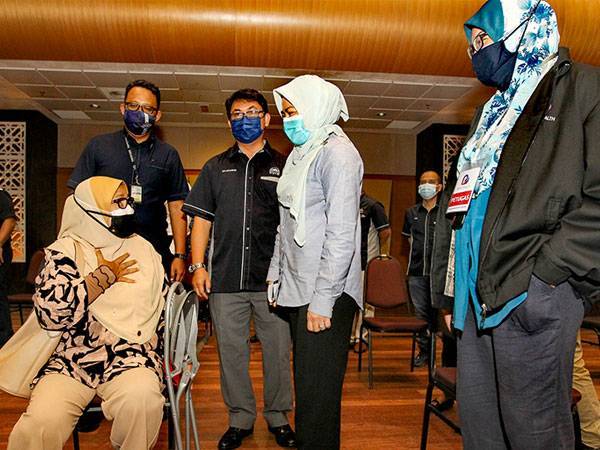 Noraini bertanya sesuatu kepada seorang wanita yang menunggu giliran untuk menerima vaksin di PPV di USIM.