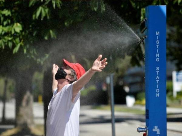 Seorang lelaki menyejukkan badan dengan air di Vancouver, British Columbia pada 29 Jun lalu. - Foto Reuters