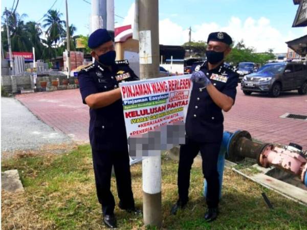 Kamarul Zaman (kiri) bersama Mohd Roze menanggalkan poster ah long yang dipasang sindiket itu di tepi jalan raya.