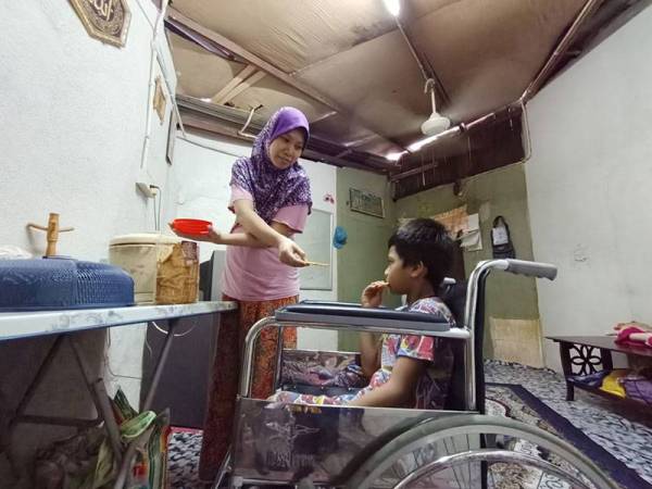 Siti Azura melayani anak sulungnya, Muhamad Farez Iqbal yang mengalami lumpuh separuh badan.