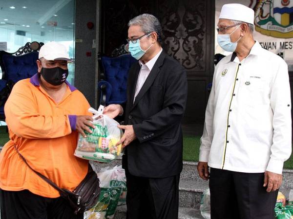 Rumaizi (tengah) menyampaikan sumbangan kepada Pengerusi Persatuan Kebajikan Usahawan Gerbang Malam, Ahmad Irwan (kiri) pada Majlis Penyampaian Sumbangan Barangan Makanan kepada wakil peniaga Gerbang Malam. - Foto Bernama