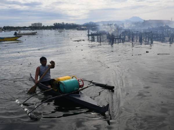 Seorang penduduk Kampung Tanjung Aru Baru membawa tong gas keluar dari kawasan kebakaran di kampung tersebut hari ini. - Foto Bernama