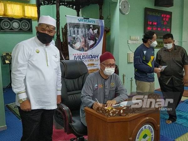 Zulkifli (duduk) menandatangani buku lawatan ketika hadir ke Program Musa’adah 3.0 di Surau Al-Faizin, Taman Serai Permai pada Selasa.
