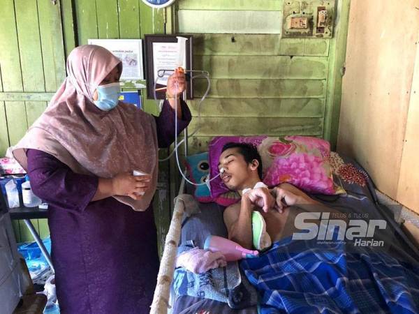 Rosliah membantu anaknya, Mohamad Edahan yang lumpuh minum air melalui tiub.