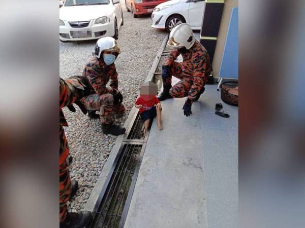 Anggota bomba membantu mengeluarkan kaki seorang kanak- kanak lelaki yang tersangkut pada celah penutup longkang di Kampung Batu 4 Kota Tinggi pada Khamis.