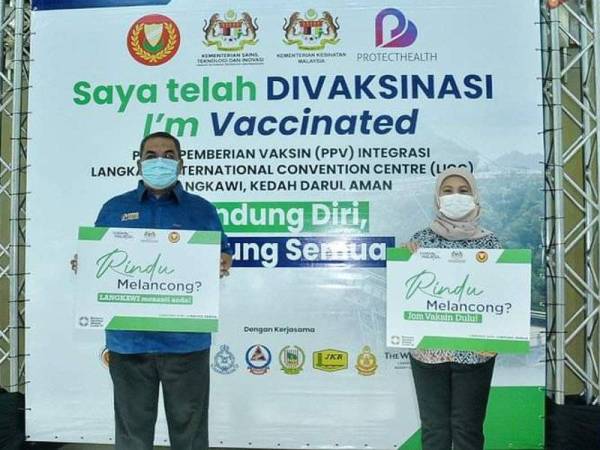 Muhammad Sanusi (kiri) dan Nancy Shukri (kanan) memegang plakad 'Jom Vaksin Dulu' ketika melakukan Lawatan Kerja ke PPV Integrasi di LICC, Langkawi pada Sabtu. - Foto Ihsan UPDA