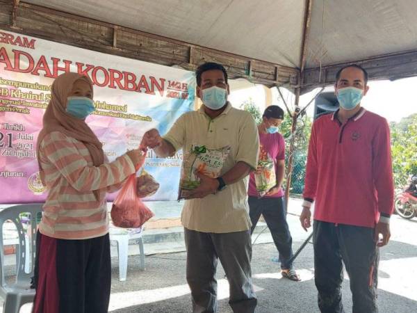 Khairul Shahril (tengah) memberikan daging kepada salah seorang penduduk yang membantu melaksanakan ibadah korban di Kampung Suak Padi, Seri Iskandar.