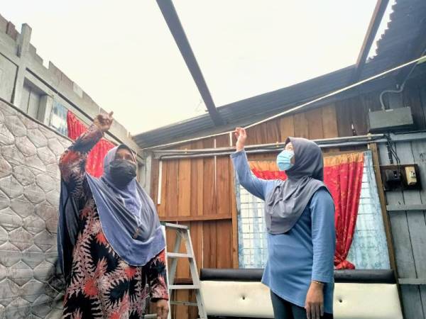 Siti Minah (kiri) dan Harmizah menunjukkan bumbung rumah mereka tercabut diterbangkan angin kencang.