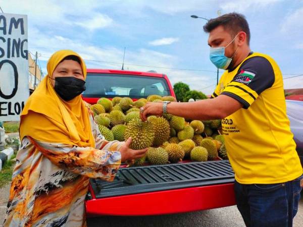 Murtadhadumizi (kanan) menyampaikan durian kepada penduduk yang melalui Jalan Kota Bharu-Pasir Pekan di sini pada Sabtu.