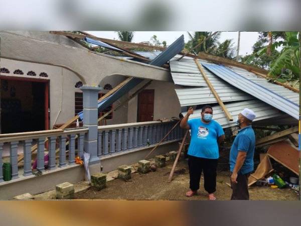 Mohd Tarmizi (kanan) meninjau keadaan bumbung rumah Mohd Ridzuan yang rosak teruk dalam kejadian ribut di Felda Sungai Panching Utara di sini pada Isnin.