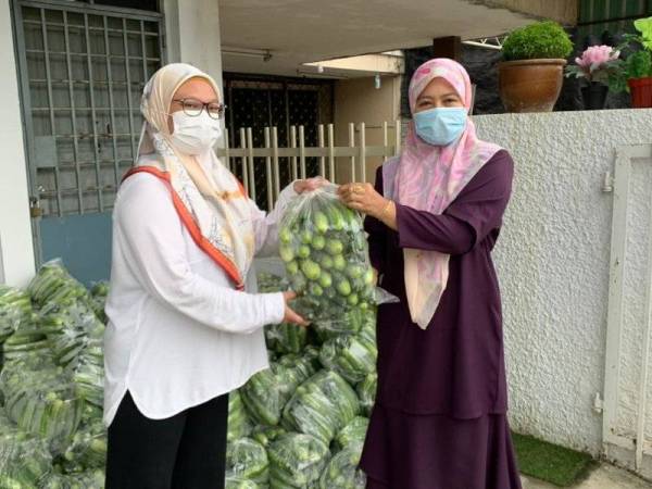 Ratna (kiri) menyampaikan bekalan timun tersebut kepada wakil-wakil masyarakat di bawah parlimen Kota Bharu.