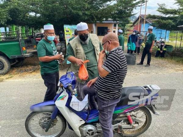 Zuridan (tengah) mengagihkan ikan patin kepada penduduk kampung pada Sabtu.