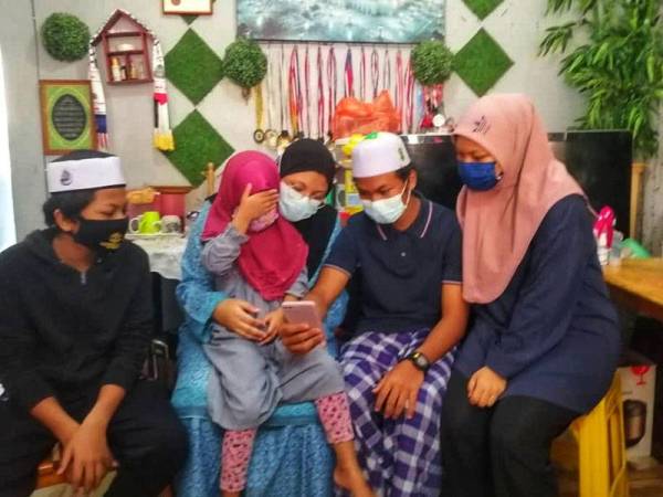 Anak bongsu, Nisa Ailani Mohd Suhaimi menutup mata sewaktu kakaknya membuka gambar arwah ibu bapanya.