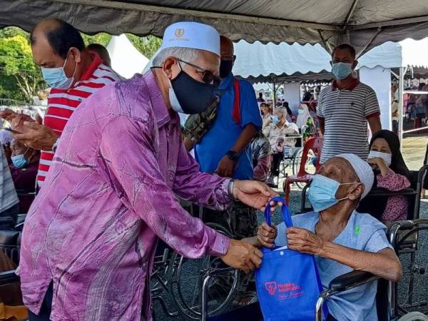 Mohd Hayati (kiri) menyerahkan cenderahati kepada seorang warga emas, Wahab Ahamad, 96 yang menerima vaksin pada Program Mobilisasi Vaksin Komuniti (Movak) Dos Dua Daerah Pokok Sena di Kampung Bukit, Pokok Sena pada Khamis.