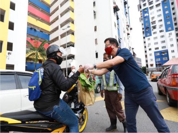 Dominic (kanan) mengagihkan barangan kepada 100 keluarga di PPR Pekan Batu, pada Khamis. 