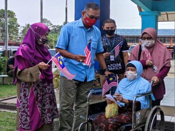 Rosol (dua dari kiri) mengagihkan bendera dan bertanya khabar penduduk yang hadir menerima vaksin di SK Tanggol pada Sabtu.