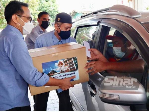 Mohd Azman (kiri) menyampaikan sumbangan kepada peniaga dan penjaja kecil secara pandu lalu pada Program Prihatin Asnaf MAIK bersama Kelab Kebajikan Cakna Kelantan di Pejabat MAIK, Lundang, Kota Bharu pada Sabtu.