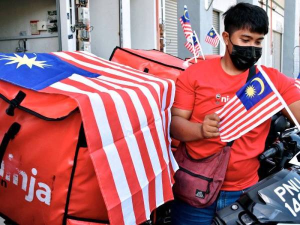 Salah seorang kakitangan syarikat kurier Ninja, Ahmad Nazrul Ahmad Nazri, 23, memasang Jalur Gemilang yang diterimanya daripada Jabatan Penerangan Melaka pada Program Info On Wheels (IOW) Merdeka di Rembia hari ini. - Foto Bernama 