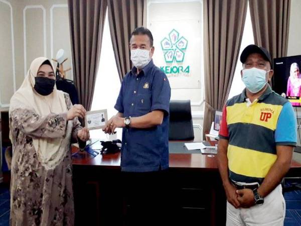 Che Zakaria (tengah) menyerahkan sumbangan kepada Bendahari JPKK Felda Air Tawar 5, Salabiah Mohd Said bagi program vaksinasi di Pejabat Kejora, Bandar Penawar, Kota Tinggi pada Ahad.