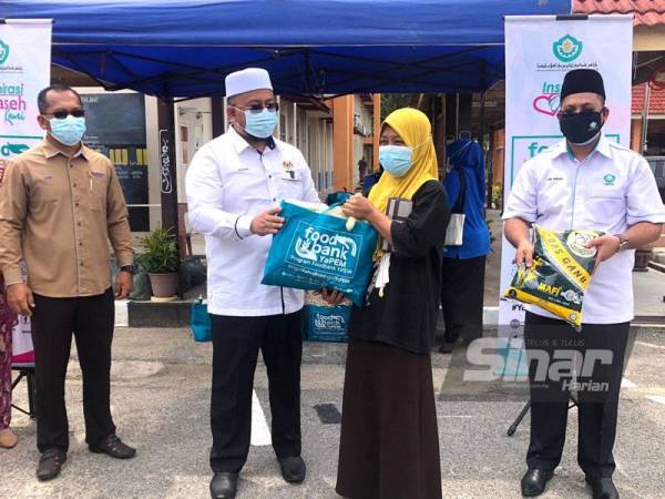 Ahmad Marzuk Shaary (dua dari kiri) menyampaikan agihan Food Bank daripada YaPEIM kepada salah seorang penerima, Rosmaini Saari, 38, di Sekolah Kebangsaan Pulau Gajah, Kota Bharu pada Ahad.