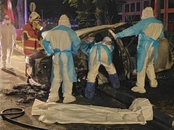 Anggota bomba yang memakai PPE sedang mengeluarkan mayat dari kereta yang terbakar dalam kejadian pada awal pagi Isnin.