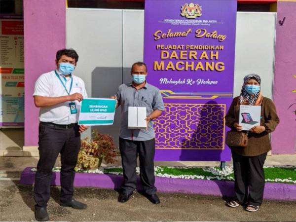 Wakil dari Petronas (kiri) menyampaikan tablet kepada 158 murid terpilih di Pejabat Pendidikan Daerah Machang.
