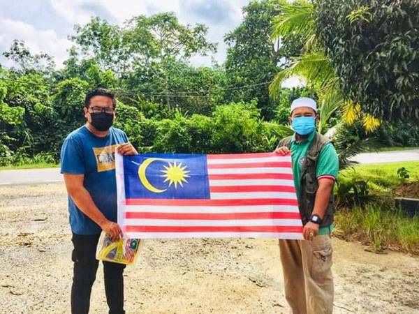 Mohd Zakhwan (kanan) menyerahkan Jalur Gemilang yang diagihkan untuk 26 JKKK di DUN Tahan.