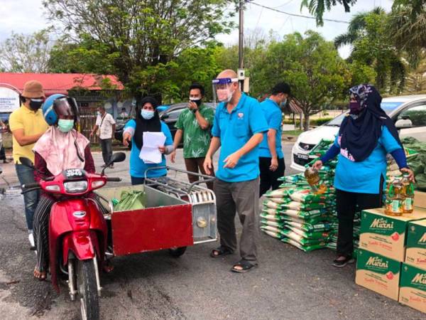 Penerima, Robaun Adawiyah Mat Yudi, 31, (dua dari kiri) menunggang motosikal roda tiga bagi mengambil sumbangan makanan daripada Pertubuhan Kraf Malaysia (MCC) yang disampaikan oleh Pengerusi MCC, Nik Faiz Nik Amin (empat dari kanan). - Foto SINAR HARIAN