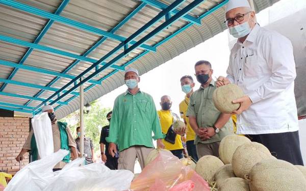 Razman (kanan) menunjukkan antara buah-buahan tempatan yang diagihkan kepada penduduk di PKPD Kampung Menteri, Kuala Sepetang.