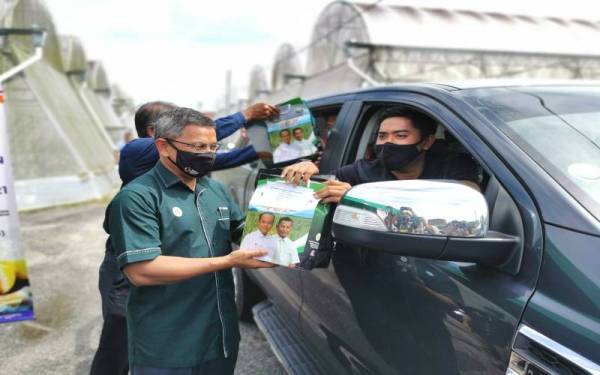 Dr Azman (kiri) menyampaikan insentif secara pandu lalu kepada Muhammad Syazwan Aiman Zakari, 26, yang merupakan salah seorang pengusaha tanaman fetigasi Melon Manis Terengganu (MMT) di Kuala Terengganu pada Ahad.