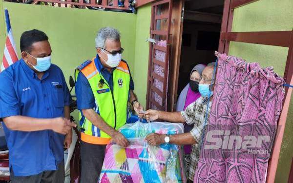 Mohd Redzuan (dua dari kiri) menyerahkan selimut dan tilam kepada salah seorang penduduk di Kampung Masjid Teluk Kumbar, Balik Pulau pada Rabu.