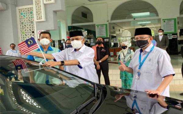 Abdul Aziz (tengah) meletakkan Jalur Gemilang pada kereta sebagai simbolik penyerahan Jalur Gemilang di Bangunan Sultan Idris Shah, di sini pada Rabu.